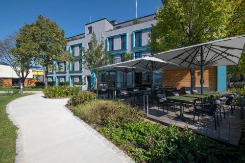 um pátio com mesas e guarda-sóis em frente a um edifício em Hotel Le Parc em Wiener Neustadt