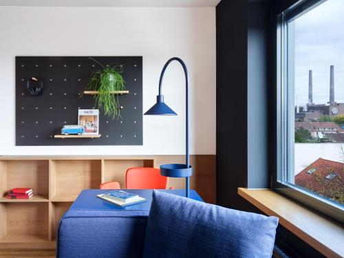 a living room with a blue chair and a window at STAYERY Wolfsburg - VW Tor 17 in Wolfsburg
