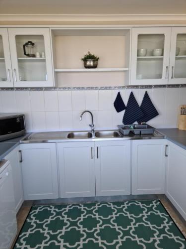 a kitchen with white cabinets and a sink and a rug at South Point Guest Lodge in Agulhas