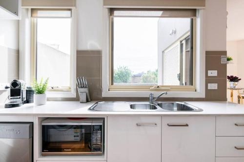 uma cozinha com um lavatório e duas janelas em Design/bright/cosy townhouse between airport &city em Melbourne