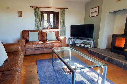 a living room with a leather couch and a television at Westdale Cottage, Elton in the Peak District in Elton