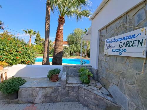 a sign in front of a building with a palm tree at Mediterranean poolside garden cottage in Kiti