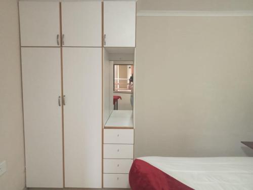 a bedroom with white cabinets and a bed and a mirror at Emampingeni lodge in Bizana