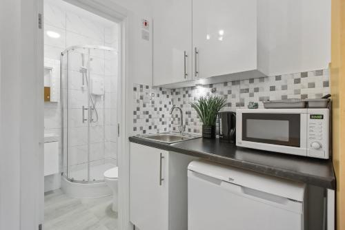 a white kitchen with a microwave on a counter at Heathrow Airport Studios with En-Suite in Southall