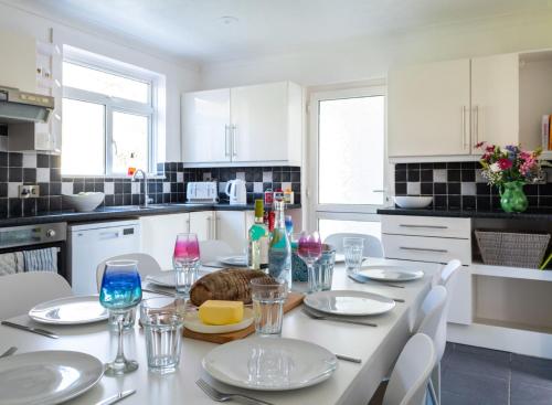 a white kitchen with a table with plates and wine glasses at WOOLACOMBE OAKLEA 4 Bedrooms in Woolacombe