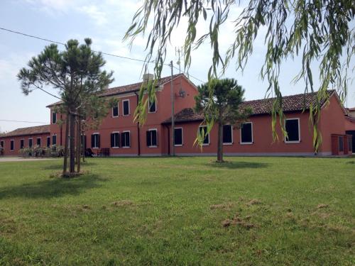 un grand bâtiment rouge avec des arbres dans un champ dans l'établissement Agriturismo Ca' Bonelli 1924, à Scardovari