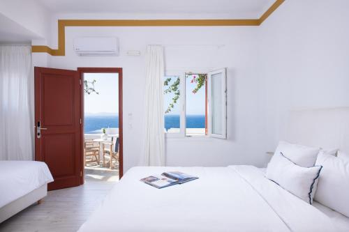 a white bedroom with a bed and a view of the ocean at Hotel Tagoo in Mýkonos City