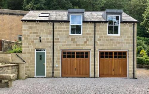 uma casa de tijolos com duas portas de garagem e uma entrada em The Coach House - *New Build in Traditional Style* em Todmorden