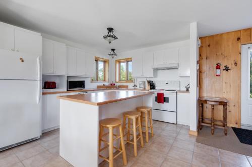 a kitchen with white cabinets and a island with bar stools at MontFJORD - Chalets, SPA et vue - ChantaFJORD #2 in Sacré-Coeur-Saguenay