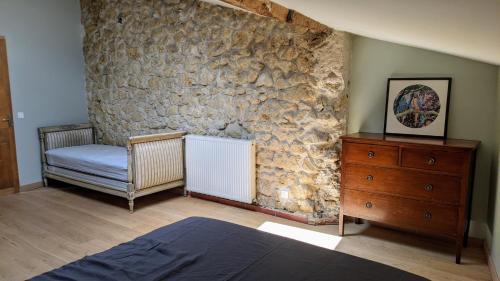 - une chambre avec un mur en pierre, un lit et une commode dans l'établissement Nicely renovated wine-grower house, à Fargues-Saint-Hilaire