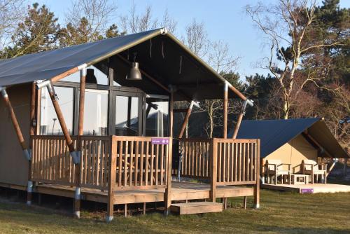 una casa con techo negro y porche en Safari Lodge, glamping aan zee!, en Callantsoog