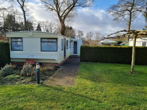 a small white caravan in a yard with a hedge at Camping Vossenberg - op de Veluwe! in Epe