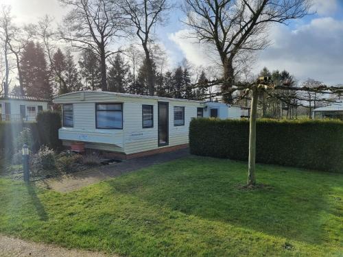 a small white caravan in a yard with a fence at Camping Vossenberg - op de Veluwe! in Epe