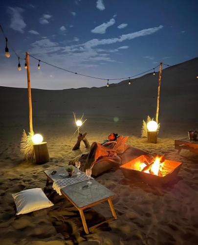 a person laying in the sand next to a fire on the beach at Duna Camp Huacachina in Ica