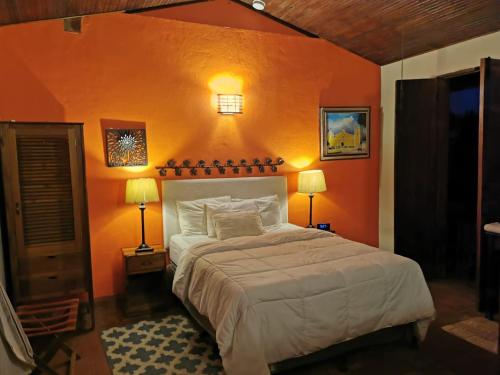 a bedroom with an orange wall with a bed and two lamps at Hotel Montecillos in San José