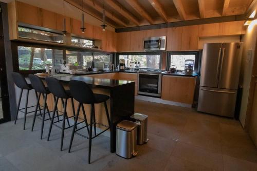 a kitchen with a bar with chairs and a refrigerator at Casa William en el bosque in Valle de Bravo