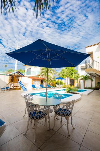a table and chairs with a blue umbrella next to a pool at Bungalows Maria Teresa in Rincon de Guayabitos