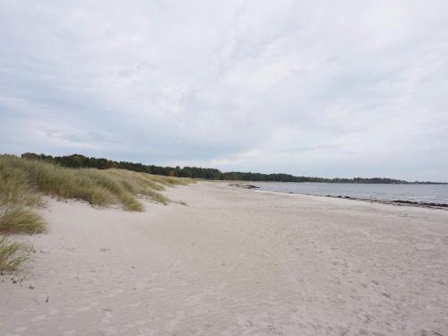 a sandy beach with grass and water on a cloudy day at 6 person holiday home in LÖTTORP-By Traum in Löttorp