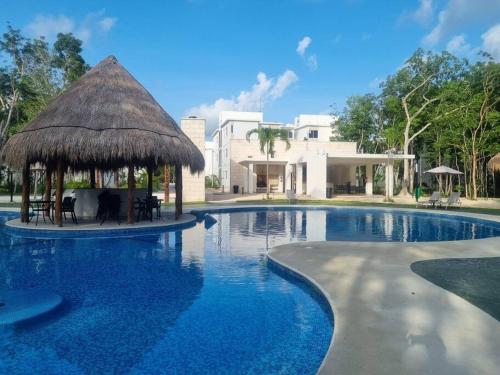 a large swimming pool with a thatch roof at Hermoso condominio con alberca en Puerto Morelos in Puerto Morelos