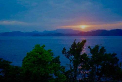 a sunset over the water with trees in the foreground at sauna×star×sea　Highland Panorama Ocean View in Shima