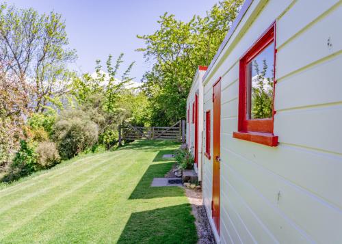 a white house with a red window and a yard at Mount Cook Station Huts in Lake Tekapo
