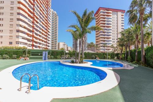 a swimming pool with palm trees and buildings at Ambar Beach in Calpe