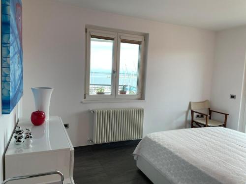 a white bedroom with a bed and a window at Costa Azzurra Aparment in Grado