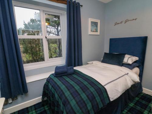 a bedroom with a bed with a blue headboard and a window at Moor Cottage in Carnforth