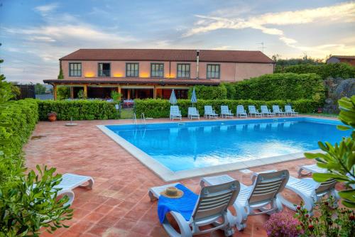 a swimming pool with chairs and a house in the background at Agriturismo Biologico Corte Aragonese in Santa Maria di Licodia