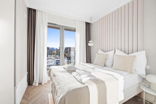 a white bedroom with a bed and a large window at GREAT Grano Residence in Gdańsk