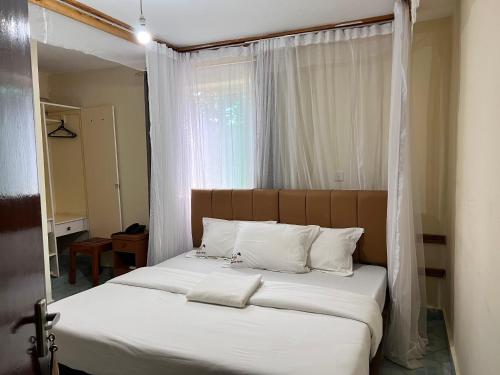 uma cama com lençóis brancos e almofadas num quarto em Lavender Garden Hotel em Tsavo