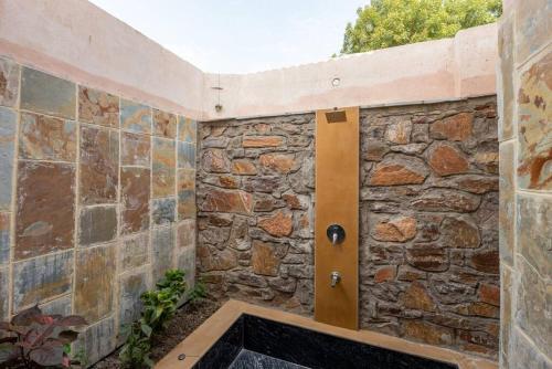 a bathroom with a stone wall with a bath tub at 1br Cottage with Pool - Eagle's Nest by Roamhome in Udaipur