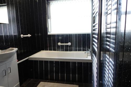 baño de azulejos negros con bañera y ventana en Stylish 3 Bedroom House Near NEC, City Centre, en Birmingham