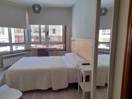 a bedroom with a bed and a table and windows at Hostal Quiper in Quiroga