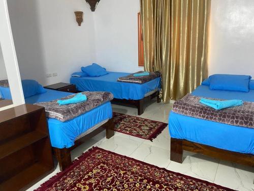 three beds in a room with blue sheets and blue pillows at Nile View Guest House in Aswan
