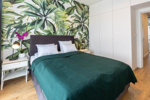 a bedroom with a green bed with a tropical wallpaper at Bielany Apart Joanny obok metra in Warsaw