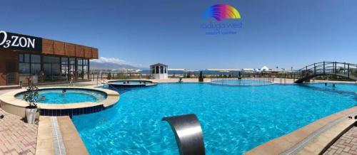 a large pool with blue water in front of a building at Raduga West Pineforest - коттедж в аренду на Иссык-Куле in Koshkolʼ