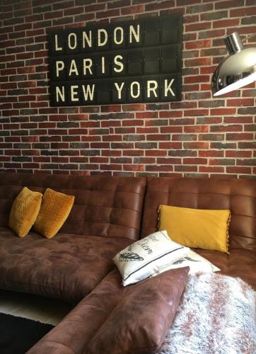 un canapé en cuir brun avec des oreillers et un panneau sur un mur de briques dans l'établissement Carpe diem, à Honfleur