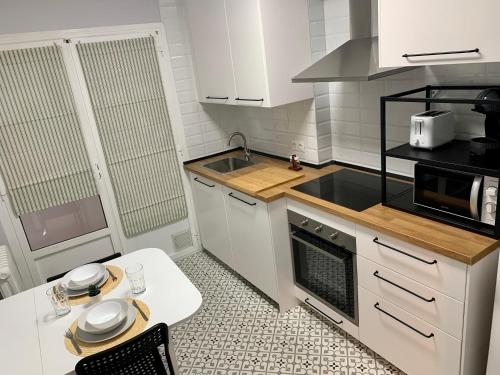 cocina con armarios blancos, mesa y microondas en Apartamento con garaje a un paso de la playa, en Gijón