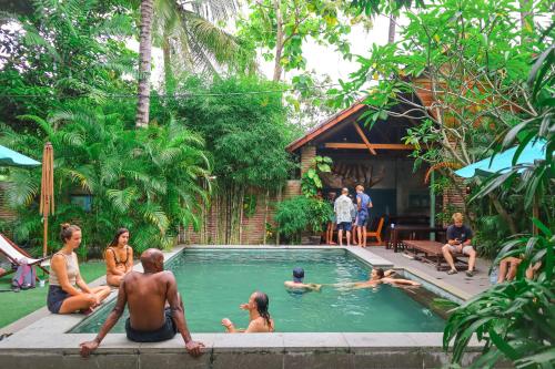 a group of people sitting around a swimming pool at Pipes Hostel in Kuta Lombok