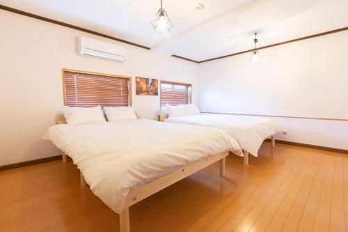 Habitación con 2 camas, paredes blancas y suelo de madera. en アブラハウス別府, en Beppu