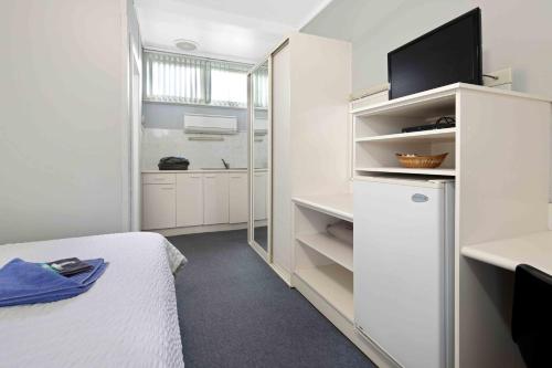 a white room with a bed and a tv in it at The Tree Motel in Narooma