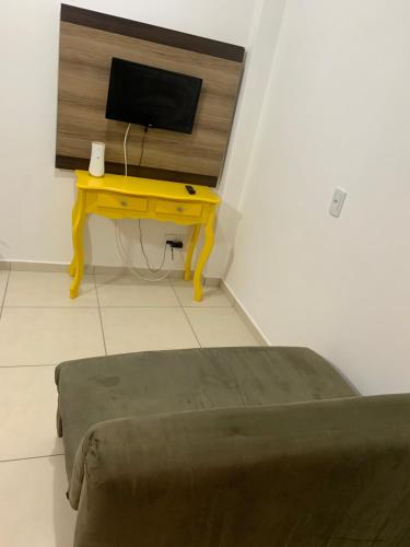 Zimmer mit einem Schreibtisch, einem TV und einem gelben Tisch. in der Unterkunft Ocean Residence in Palhoça