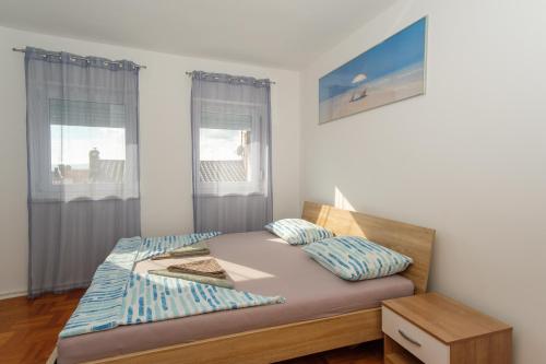 a bedroom with a bed with a nightstand and two windows at Apartment Molnar Crikvenica in Crikvenica