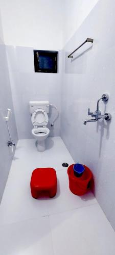 a white bathroom with a toilet and a red stool at Nilam Guest House in Bodh Gaya