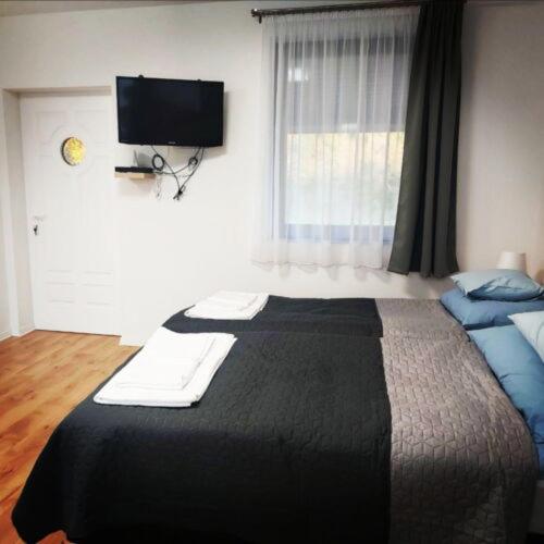 a bedroom with a large bed with a television on the wall at Kis Ház Apartman in Szigetvár