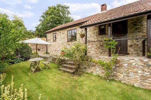 a stone house with a table and an umbrella at Holly Cottage in Honiton