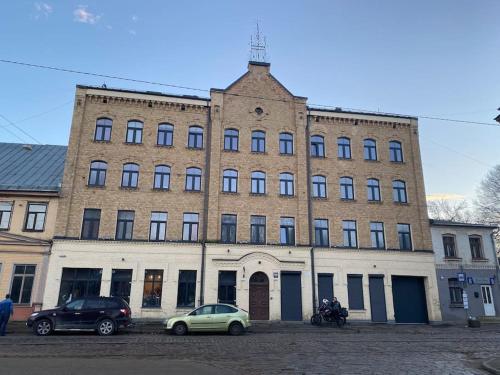 un grand bâtiment en briques avec des voitures garées devant lui dans l'établissement 1-bedroom loft in Siena Tirgus, à Riga