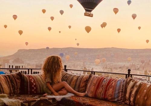 uma mulher sentada num sofá a ver balões de ar quente em Osmanli Cappadocia Hotel em Goreme