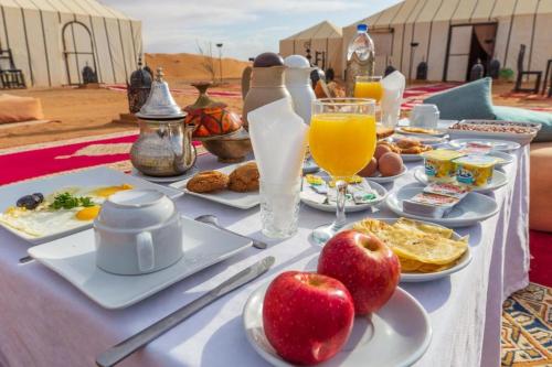 einen Tisch mit Speisen, Getränken und Äpfeln darauf in der Unterkunft Ahlam Luxury Camp in Merzouga